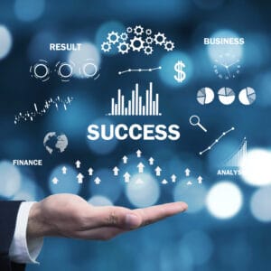Hand holding business success icons with charts, graphs, gears, and financial symbols on a blue bokeh background.