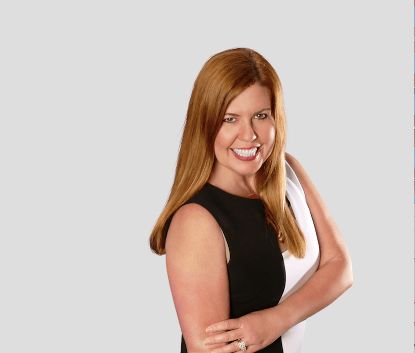 Smiling woman with long hair in black and white dress, professional headshot on a light gray background.