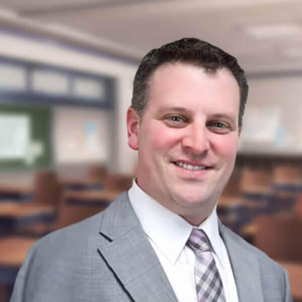 Smiling man in a suit standing in an empty classroom, educational setting, professional environment.
