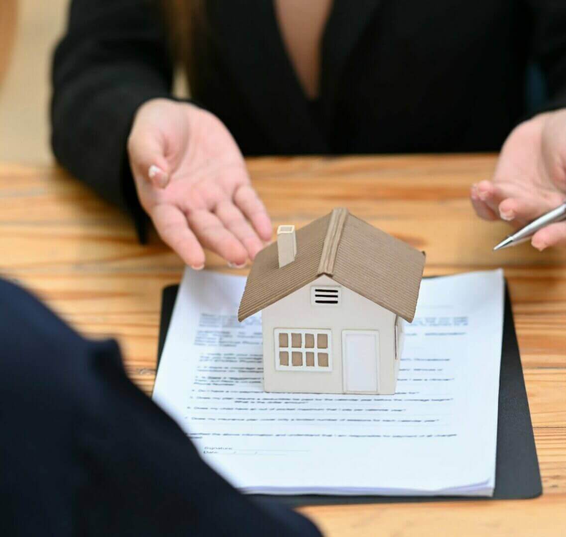 Real estate agent consulting with client, discussing property investment over house model and documents.