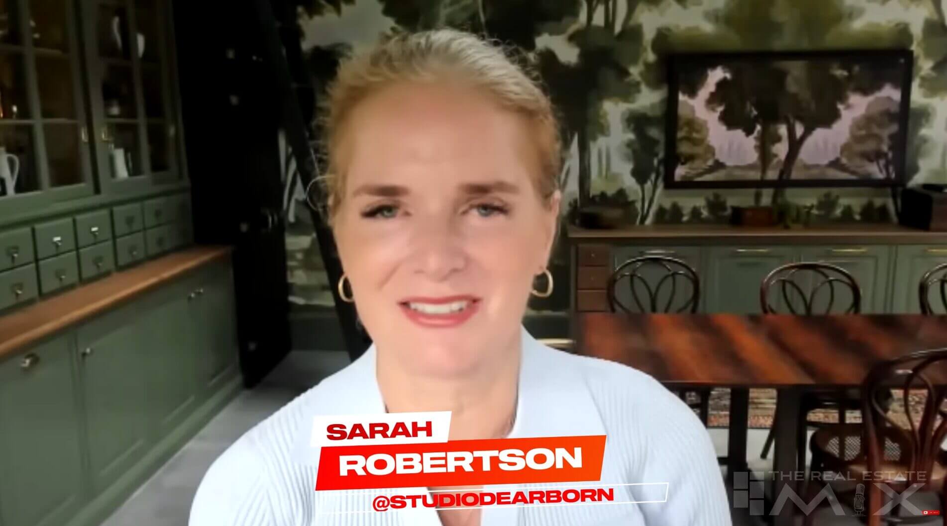 Woman smiling in stylish kitchen with green cabinets, wooden table, and forest mural. Text overlay: "Sarah Robertson @StudioDearborn".